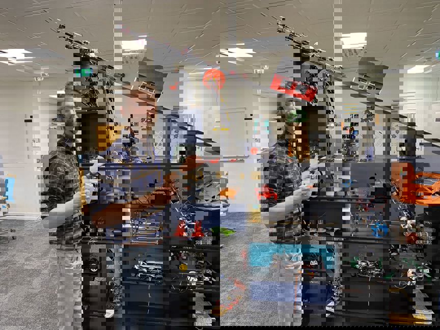 person med kaffekopp framför hylla med tekniska prylar